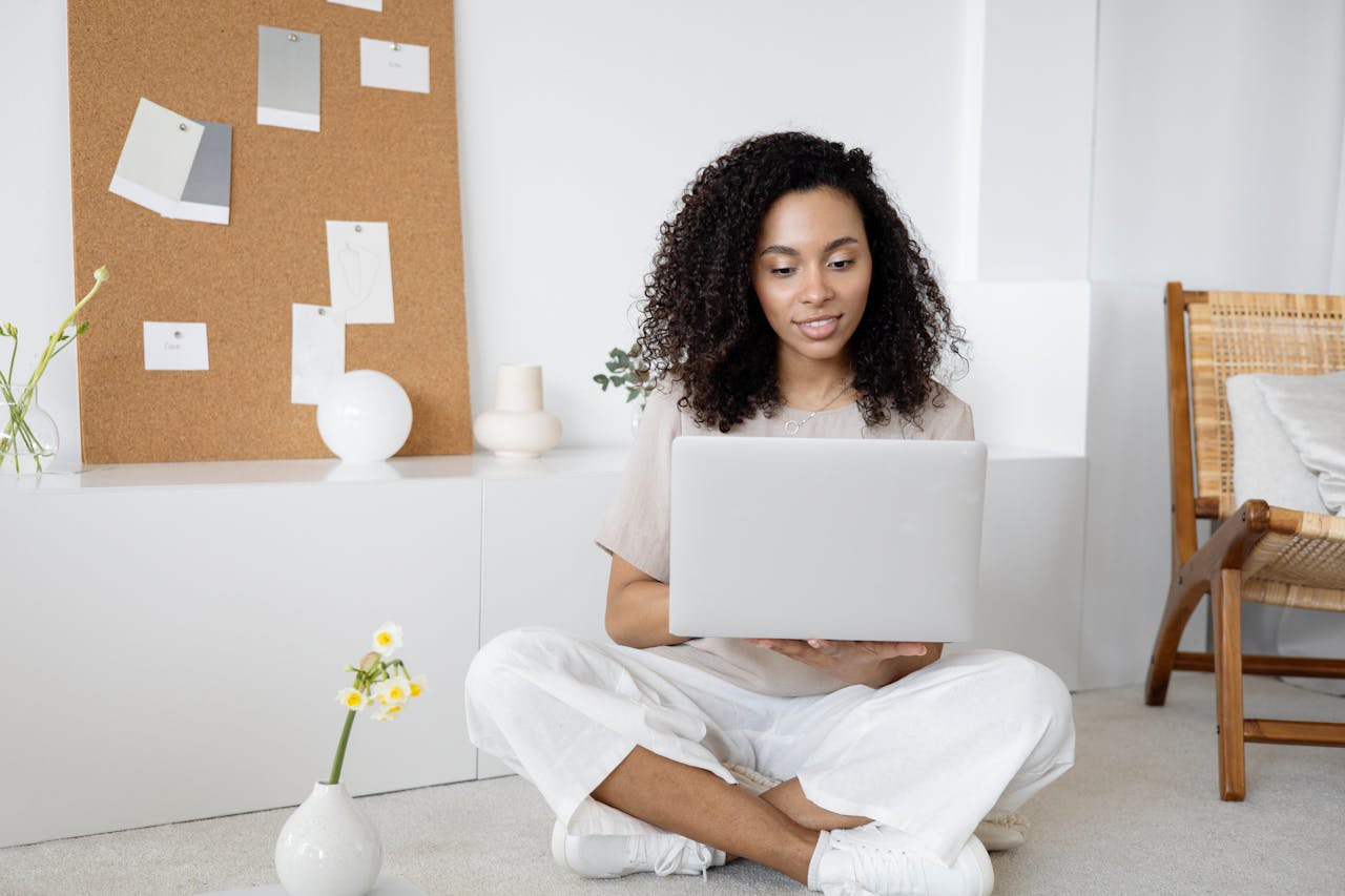 why-choose-us Young woman with curly hair working on her laptop in a cozy home setting, exuding confidence and focus.