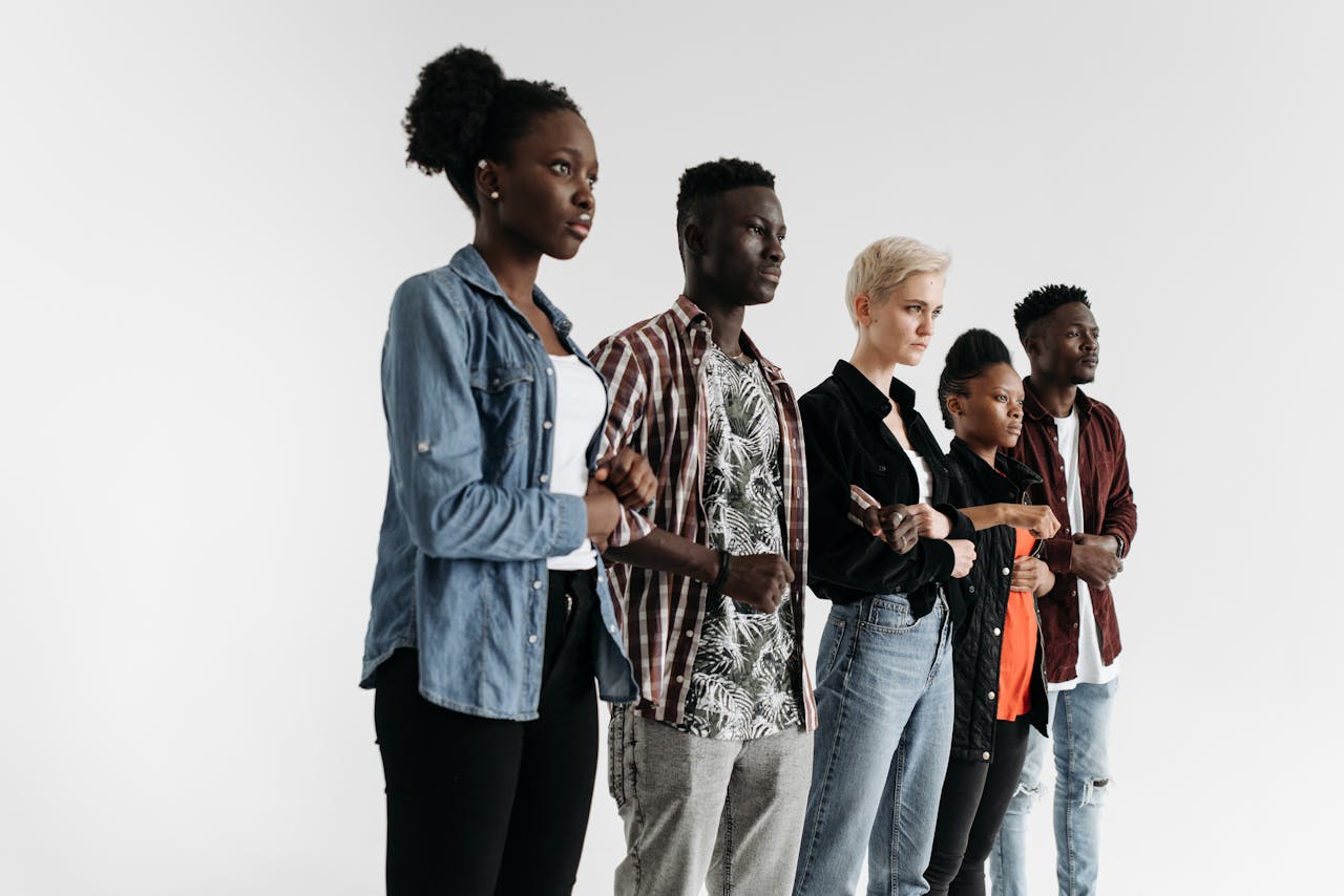Diverse group of young adults posing in studio against white background linking arms.
